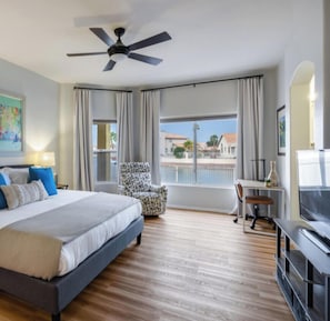 A hotel room with a bed, a desk, a chair, a TV, and a balcony with a view of buildings. - Lake Haven + Heated Pool, Dock & Pontoon Boat (Glendale)