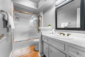 A modern bathroom with a glass-enclosed shower, a white sink with gold faucets, and a large mirror.