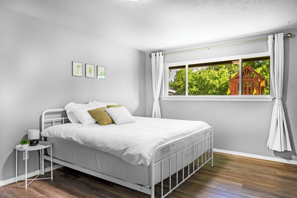 A bedroom with a white metal bed, a small bedside table with a lamp, and a window with curtains. - 🌟Family-Friendly 4BR🛝Close to All DFW Attractions🌟 (Carrollton)