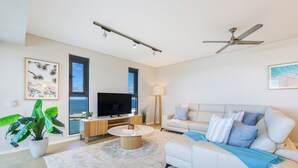 A living room with a TV, sofa, coffee table, and large windows. - Darwin Waterfront Penthouse  (Darwin)