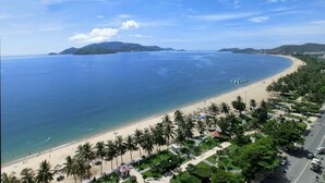 A coastal road lined with palm trees and beach huts, leading to a sandy beach with clear blue waters and distant islands. - Sea Soul Hotel (Nha Trang)