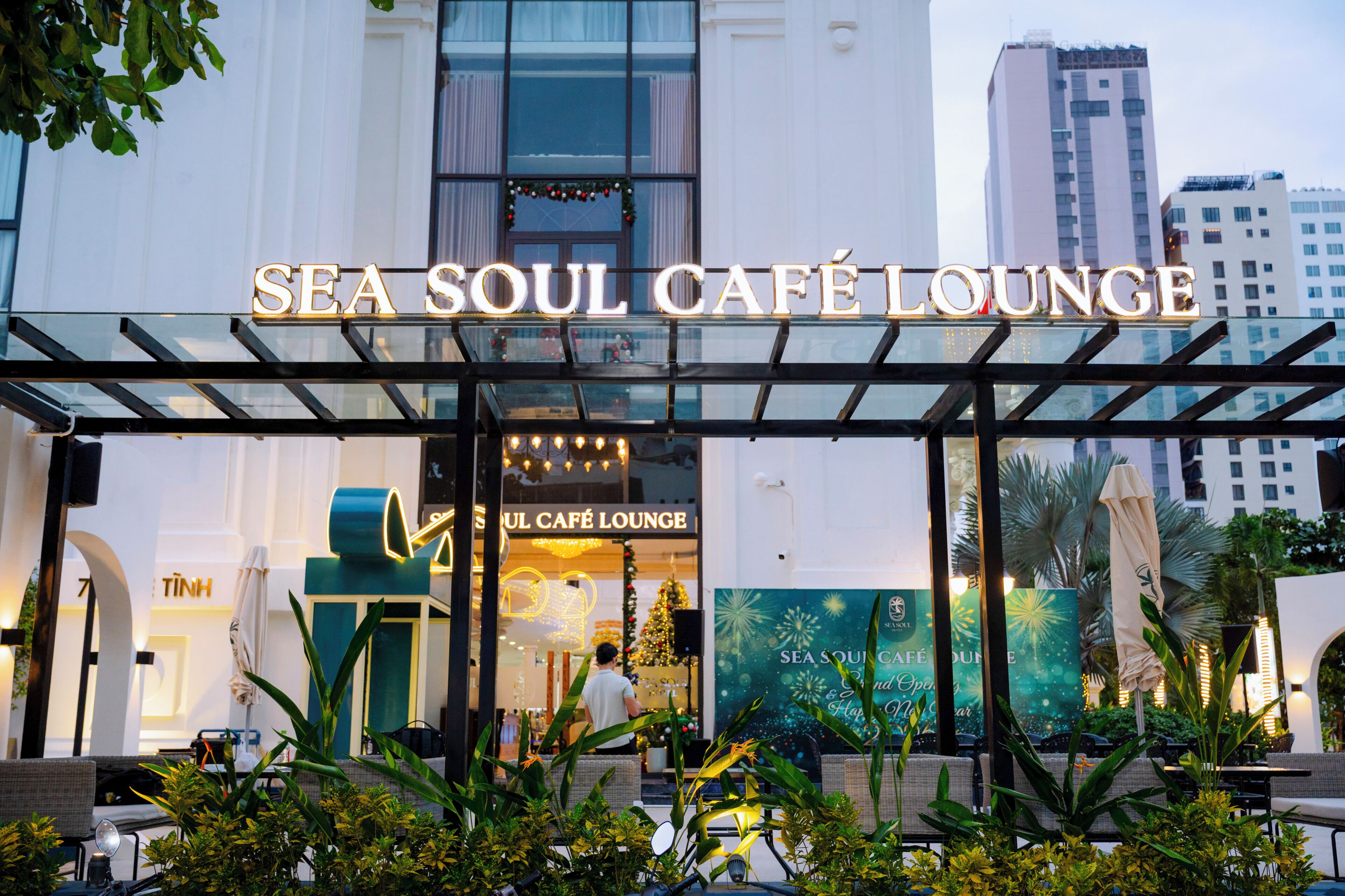 Exterior del Sea Soul Café Lounge con una cubierta de vidrio, mesas al aire libre y un adorno navideño.