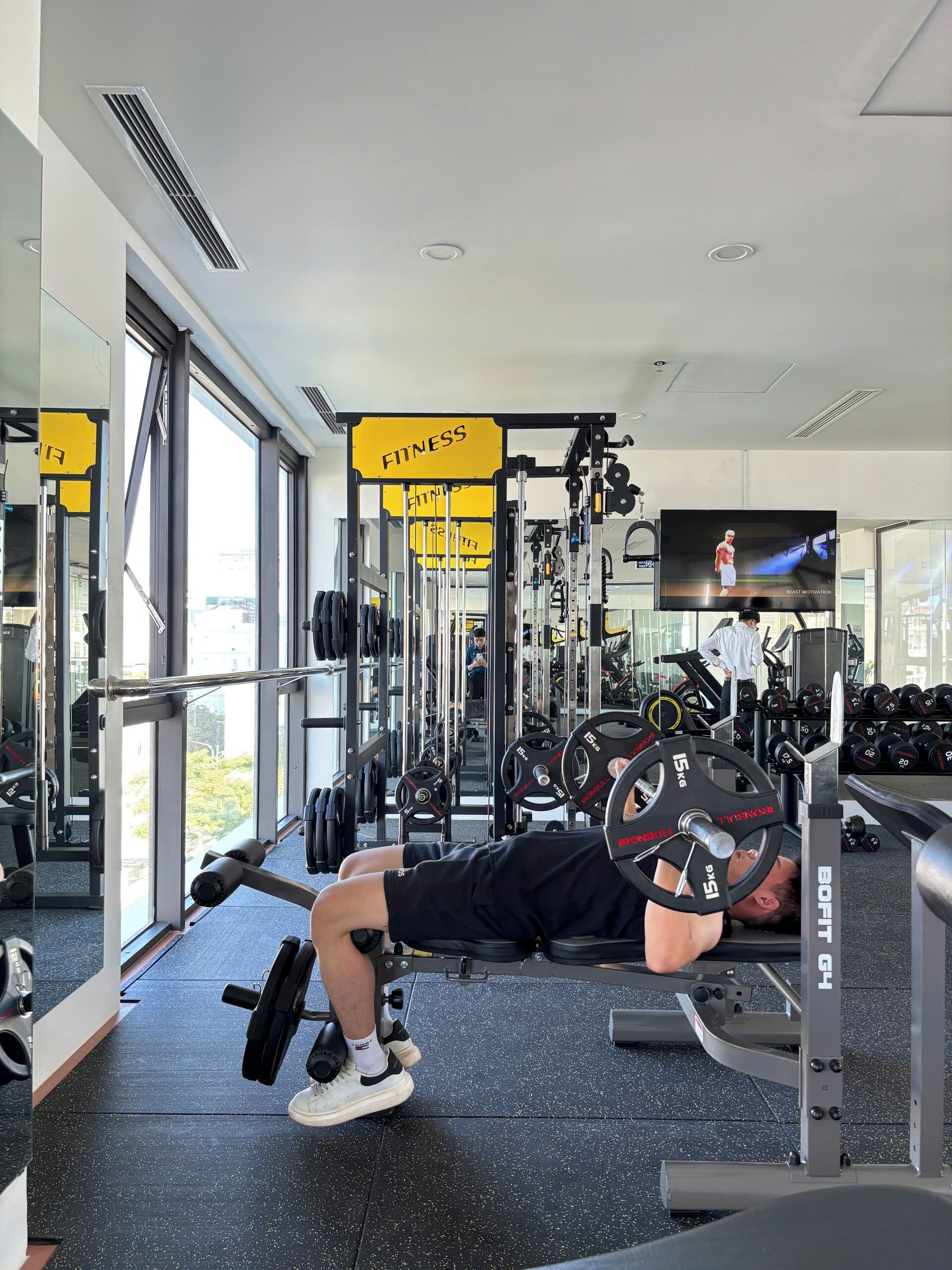 A gym with weightlifting equipment, mirrors, and a television screen.