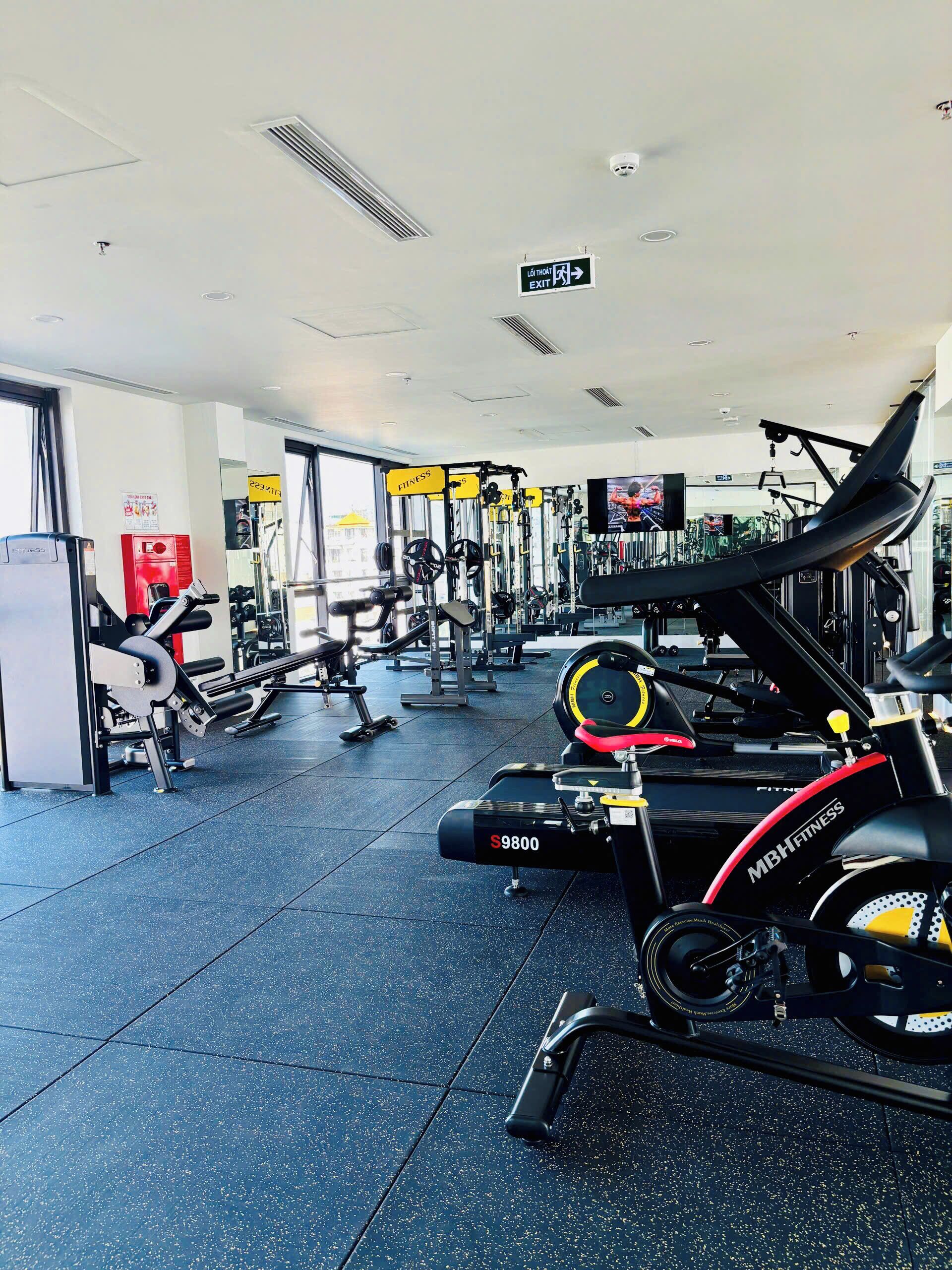 A gym with cardio machines, weightlifting equipment, and a TV screen.
