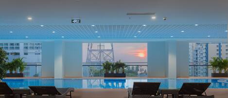 A poolside area with lounge chairs, a view of a sunset, and a crane structure in the background.