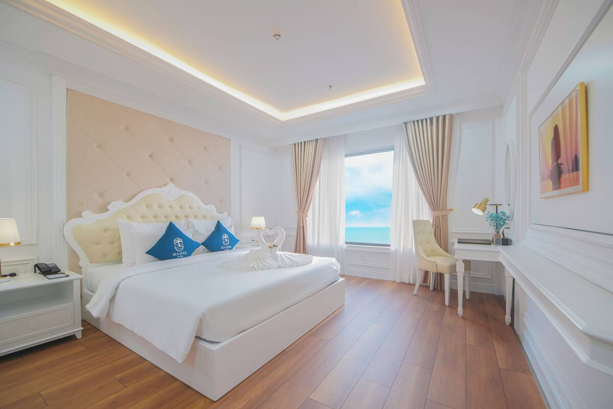 A hotel room with a large bed, a desk, and a view of the sea.