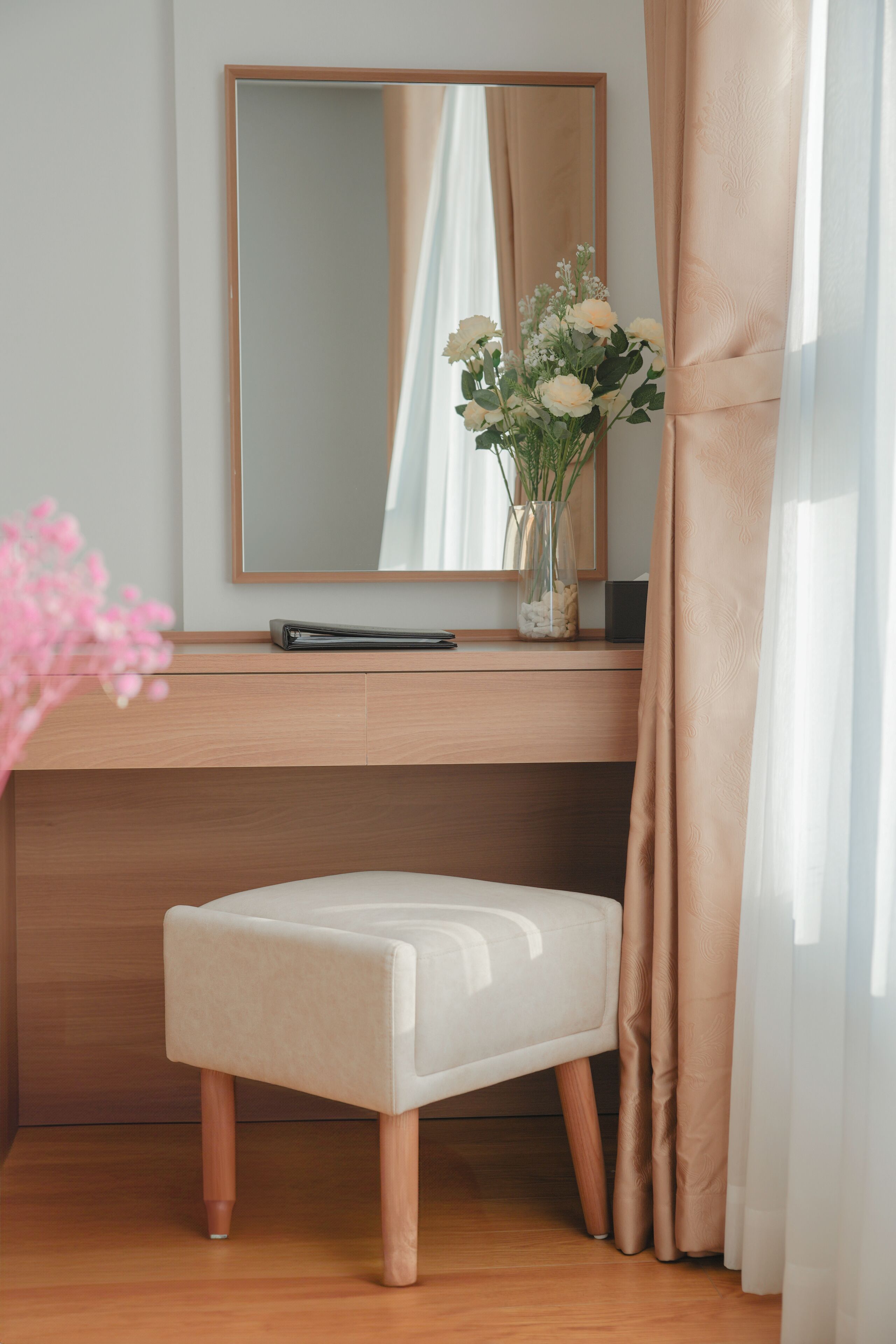 Une chambre moderne avec un bureau en bois, un miroir, un vase de fleurs et un petit tabouret.