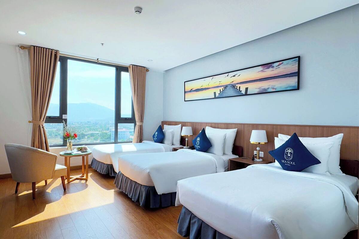 A hotel room with two beds, a desk, a chair, and a large window with a view.