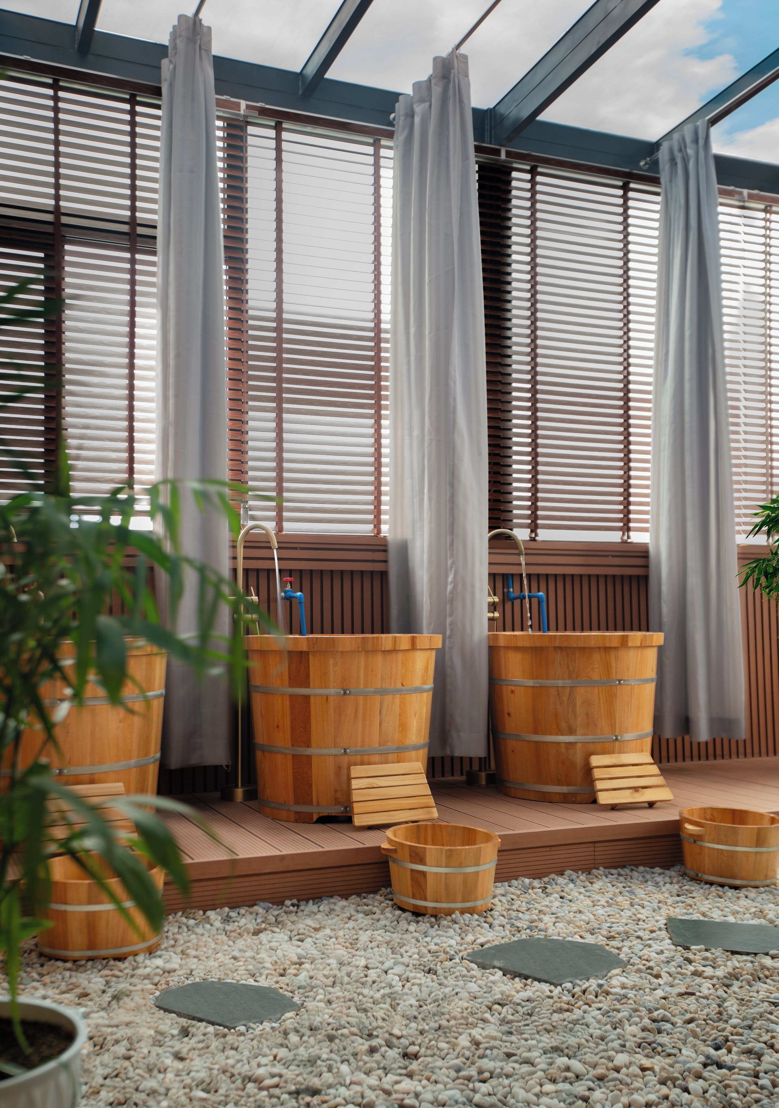 A greenhouse with wooden barrels, a water fountain, and a pebbled floor.