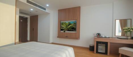 Una habitación de hotel moderna con una cama grande, un televisor montado, un escritorio con cafetera y un refrigerador pequeño.