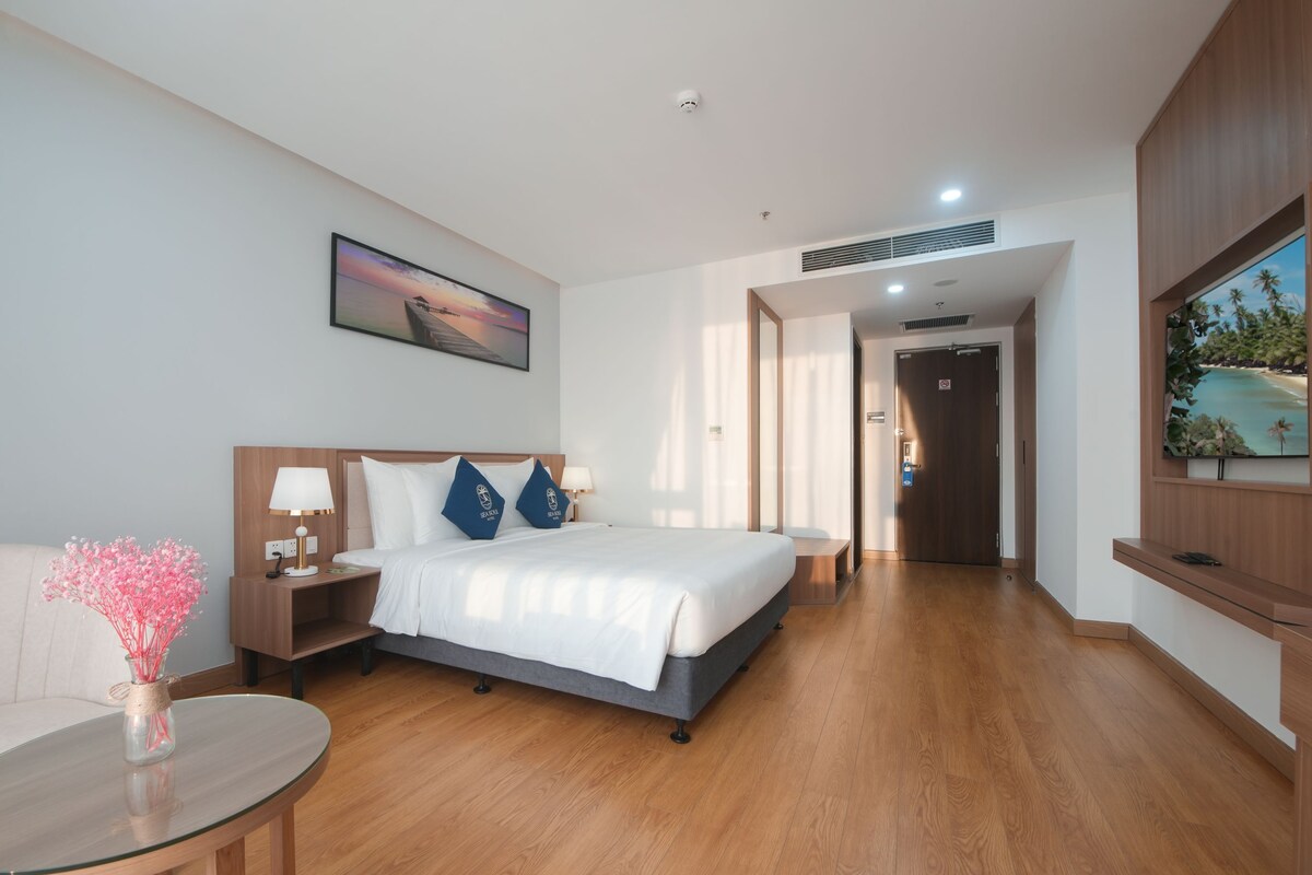 A hotel room with a bed, bedside table, lamp, and a painting on the wall.