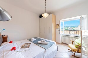 Un dormitorio con cama, una mesita de noche, una silla, un ventanal con vistas y una lámpara colgante.