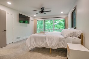 A bedroom with a bed, a ceiling fan, a TV, and a window with a view of trees. - Spacious Riverfront Delaware Home w/ Views (Delaware)