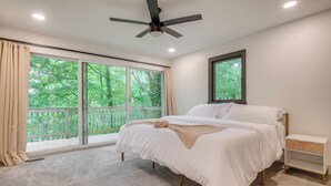 A bedroom with a bed, a nightstand, a ceiling fan, and a large window with a view of greenery. - Spacious Riverfront Delaware Home w/ Views (Delaware)