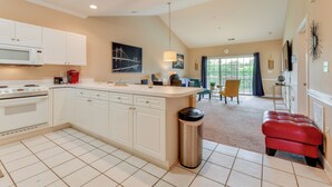 A modern kitchen with white cabinets, a stainless steel trash can, and a red leather ottoman.