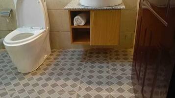 Baño con inodoro, lavamanos y un pequeño estante con una toalla.
