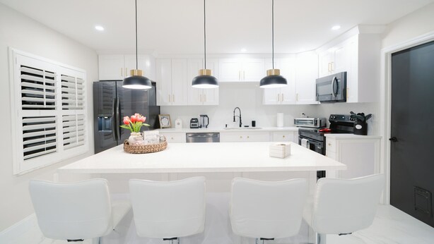 A modern kitchen with white cabinetry, a central island with bar stools, and pendant lighting. - Close to the Beach and 5th Ave! Fun Naples Peaceful Getaway 4U!  (Naples)