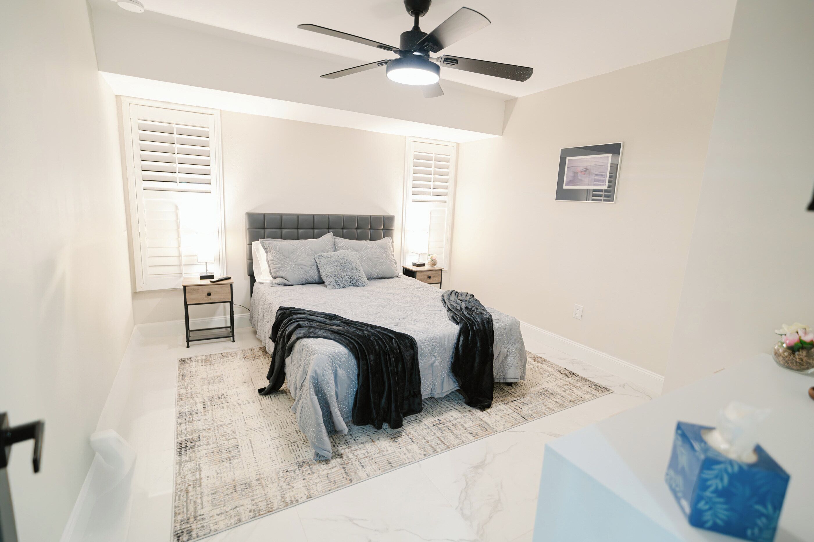 A bedroom with a bed, a ceiling fan, a nightstand, and a bedside table.