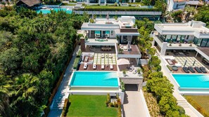 A modern resort with multiple swimming pools, outdoor seating areas, and lush greenery.