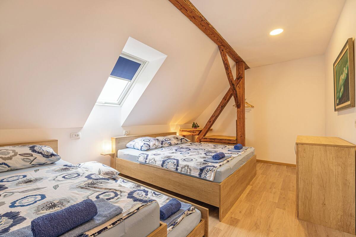 A bedroom with two beds, a skylight, wooden beams, and a small cabinet.
