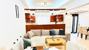 Sala de estar con sofá, mesa de centro, mesa de comedor para dos personas y una cocina al fondo.