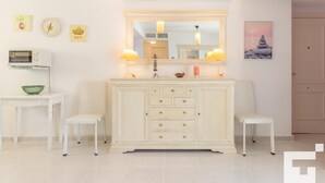 A modern bathroom with a white vanity, two chairs, a microwave, and decorative wall art.