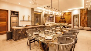 Een moderne keuken met een centraal kookeiland, een eetgedeelte met ronde tafels, en een woonkamer met een bank en decoratieve wandkunst.