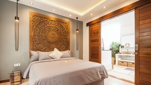 Een moderne slaapkamer met een groot bed, een decoratief wandpaneel en een houten schuifdeur naar een badkamer.