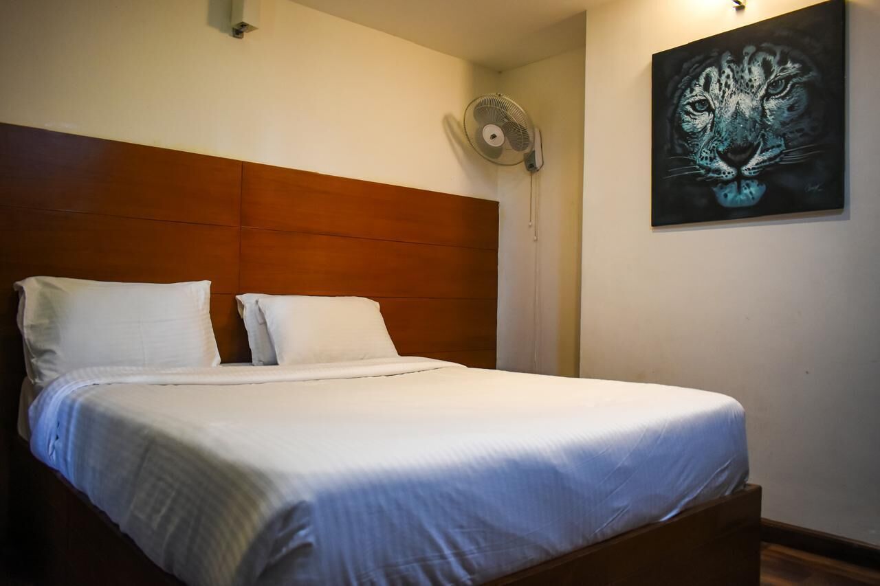 A neatly made bed with white linens, a wooden headboard, and a wall-mounted fan.