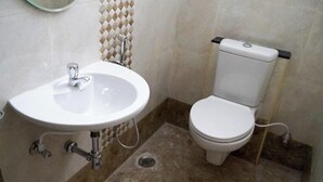 A bathroom with a white sink, a toilet, and a tiled wall. - Leopard Rock Wilderness Resort Ooty by VOYE HOMES (Ootacamund)