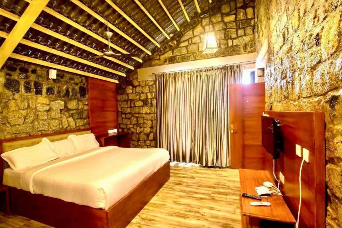 A bedroom with a stone wall, a wooden ceiling, a bed, a desk, and a TV.