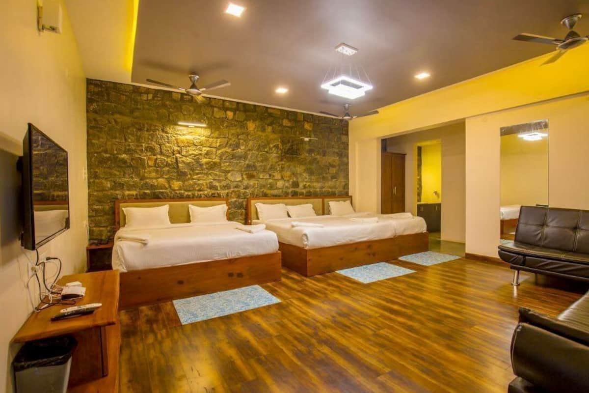 A hotel room with two beds, a wooden floor, a stone wall, a ceiling fan, and a TV.