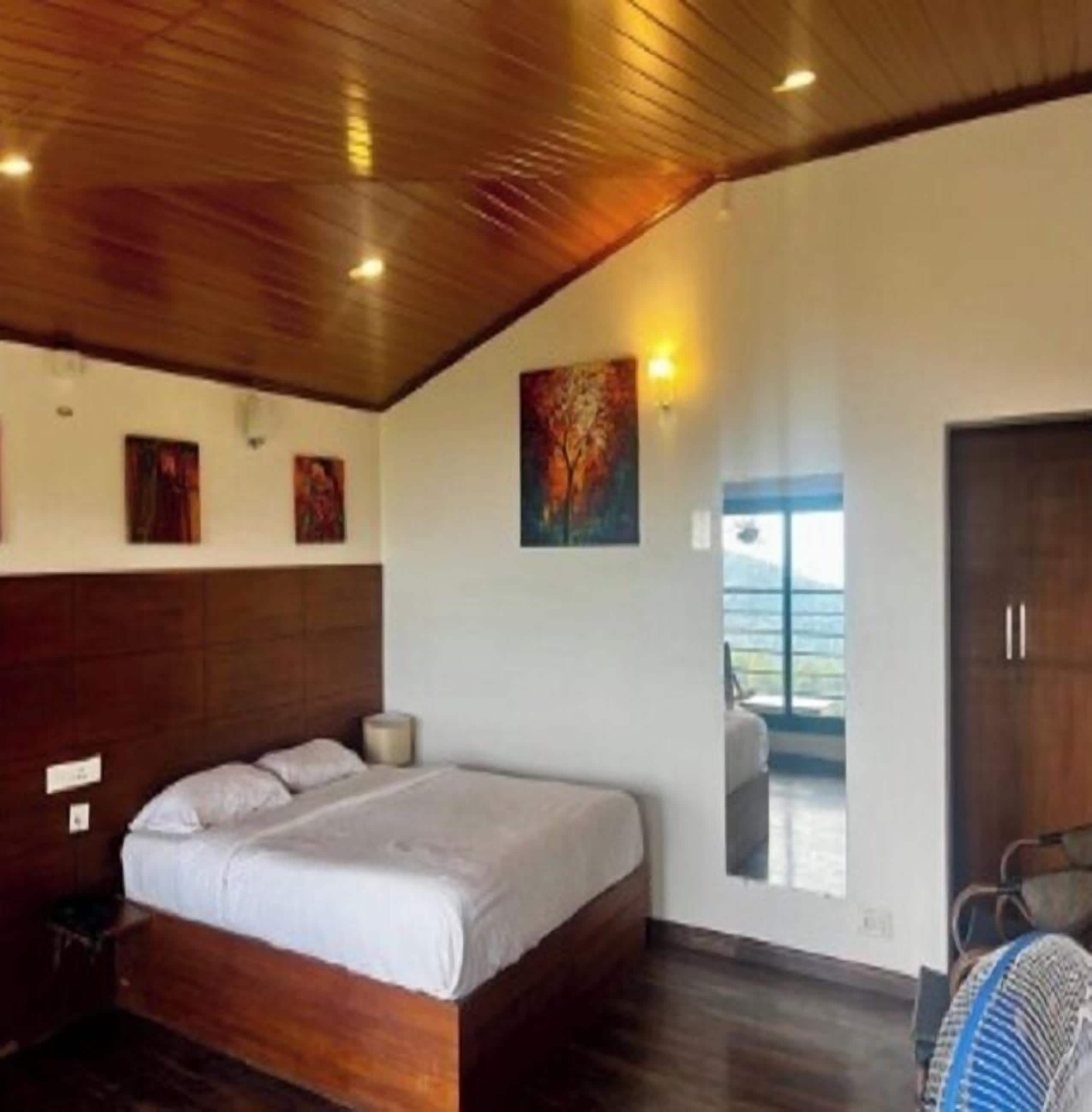 A bedroom with a wooden ceiling, a large bed, a window with a view, and artwork on the walls.
