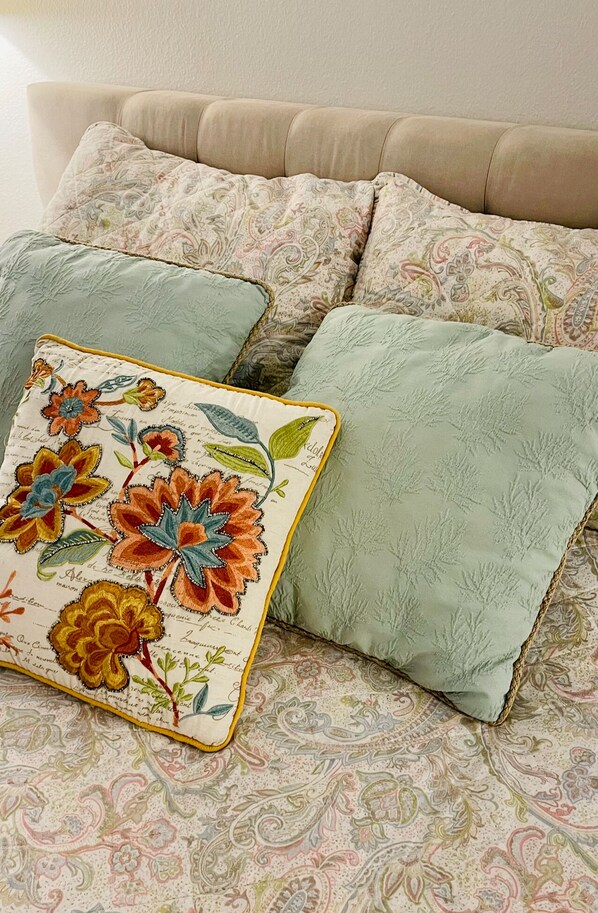 A bed with multiple pillows, one with a floral pattern and another with a paisley design.