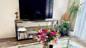 A living room with a glass coffee table, a sofa, a bookshelf, a television, and a potted plant. - New Marina Del Rey 1 BDR Beach / Pool & Hot Tub, Ocean
 (Marina del Rey)