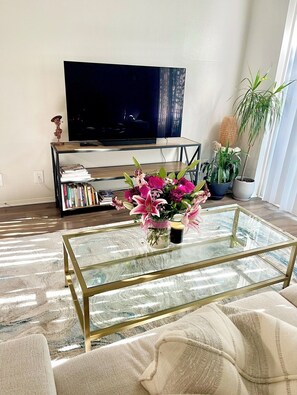 A living room with a glass coffee table, a sofa, a bookshelf, a television, and a potted plant. - New Marina Del Rey 1 BDR Beach / Pool & Hot Tub, Ocean
 (Marina del Rey)