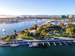 Un puerto deportivo con varios muelles y barcos, rodeado de vegetación y edificios urbanos.