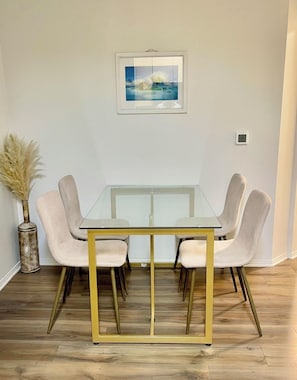 Une table à manger avec quatre chaises, un vase contenant de l’herbe des pampas et un tableau encadré accroché au mur.