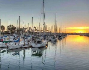 Un puerto deportivo con varios veleros amarrados en aguas tranquilas durante la puesta de sol.