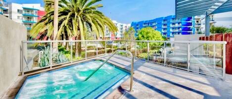 Una piscina con barandilla de vidrio, rodeada de palmeras y edificios modernos.