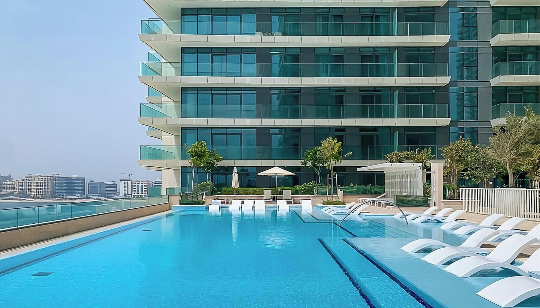 A modern hotel with a rooftop infinity pool, multiple balconies, and a view of the city skyline.
