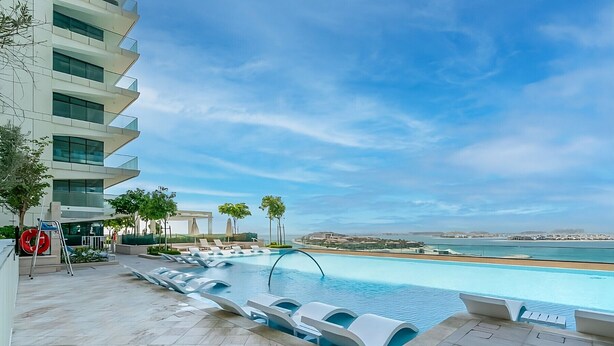 Area piscina moderna con vista sul mare, sedie a sdraio e cielo sereno.