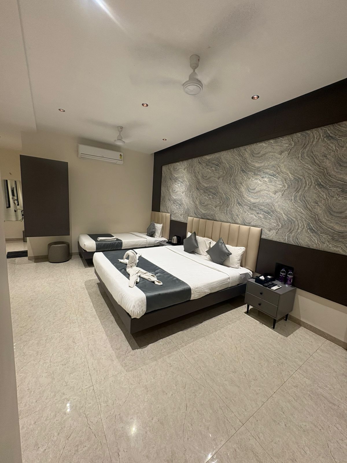 Una moderna camera d'albergo con un ampio letto, un comodino, un condizionatore d'aria a parete e una ventola a soffitto.