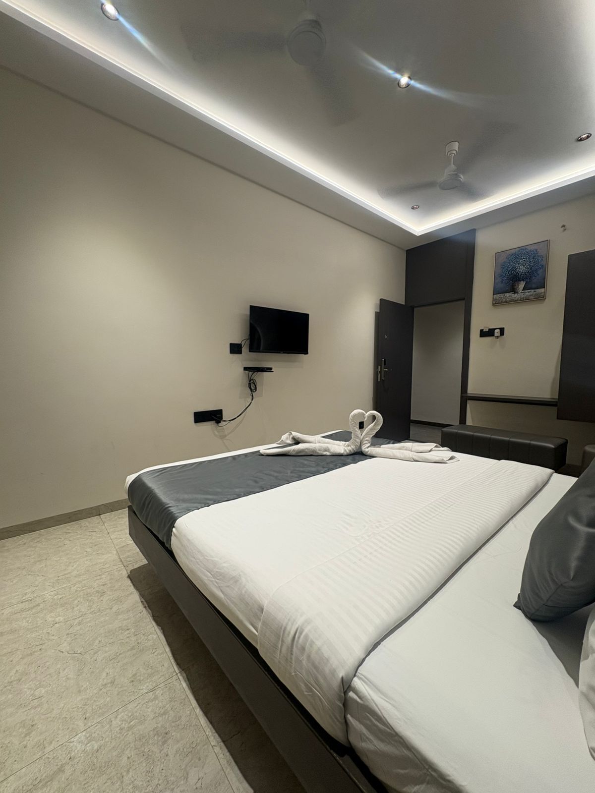 A modern hotel room with a bed, a flat-screen TV, a ceiling fan, and a painting on the wall.