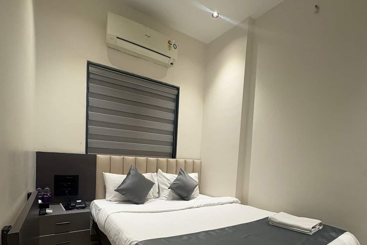 Ein modernes Schlafzimmer mit Bett, Nachttischen, einer wandmontierten Klimaanlage und einem Fenster mit Jalousien.