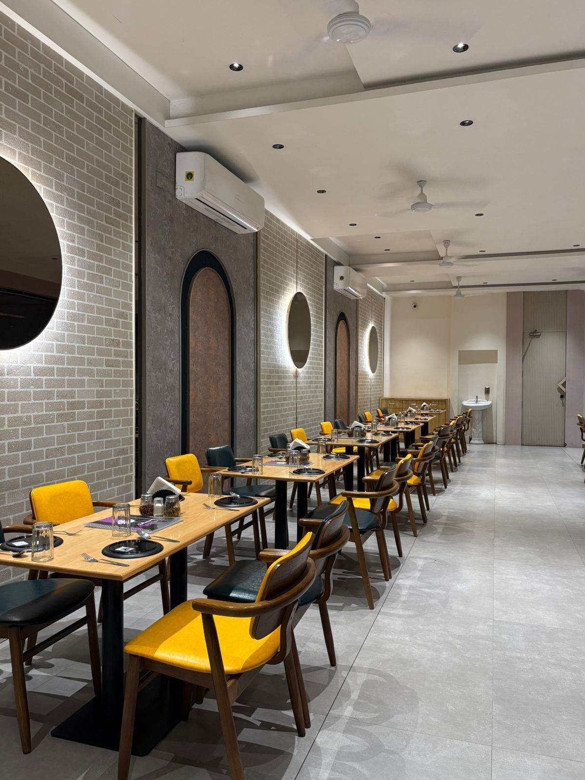 Un amplio comedor con múltiples mesas y sillas, unidades de aire acondicionado en las paredes y un ventilador de techo.