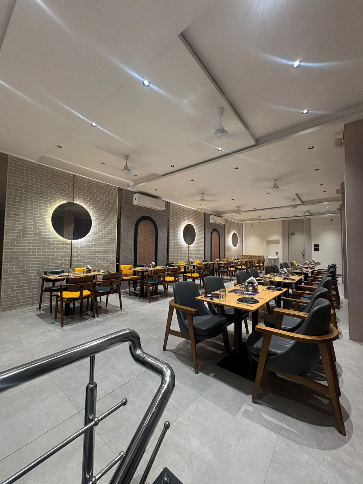 A spacious dining area with multiple tables and chairs, a brick wall, and a staircase.