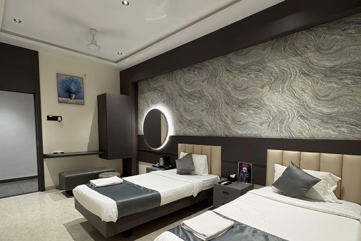 Ein modernes Hotelzimmer mit zwei Betten, einem großen, an der Wand montierten Spiegel, einem Deckenventilator und einem Boden aus Marmorfliesen.