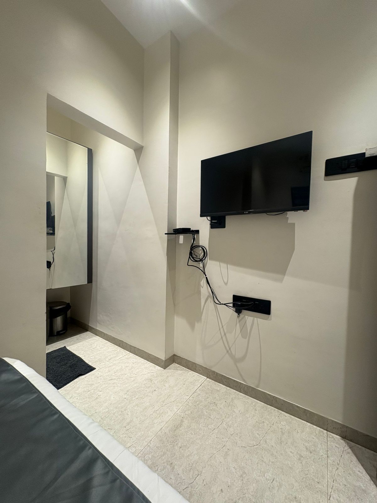 Un dormitorio moderno con una cama, un televisor montado en la pared y un cubo de basura pequeño.