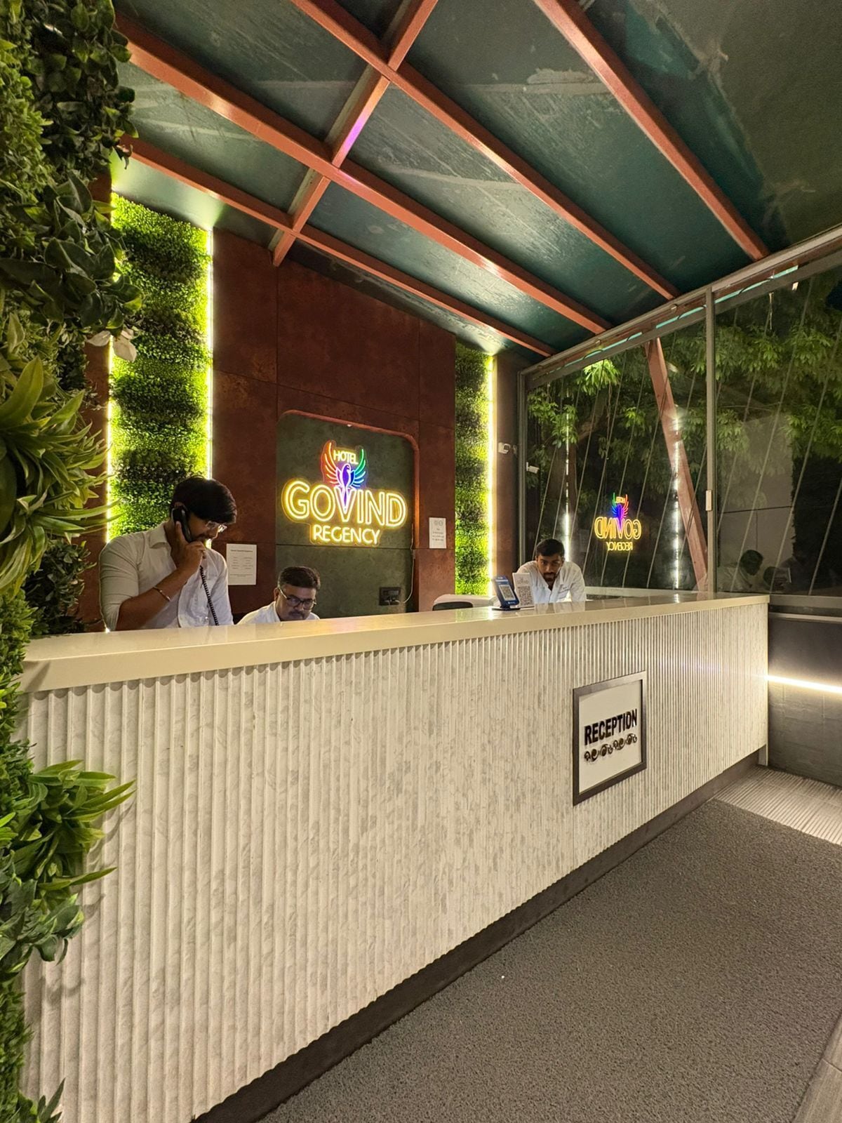 Un mostrador de recepción de hotel con un letrero de neón, un área de recepción y una señalización que indica la recepción.
